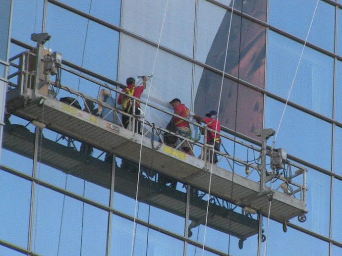 Three men installing a window graphic on a skyscraper.